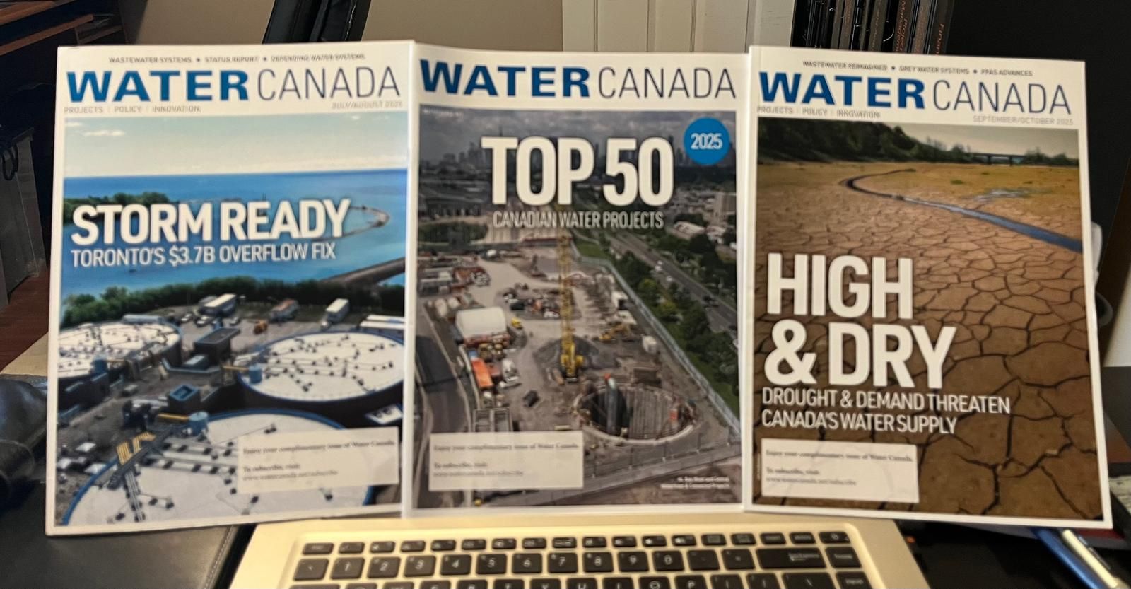 Three issues of Water Canada magazine propped up behind a laptop